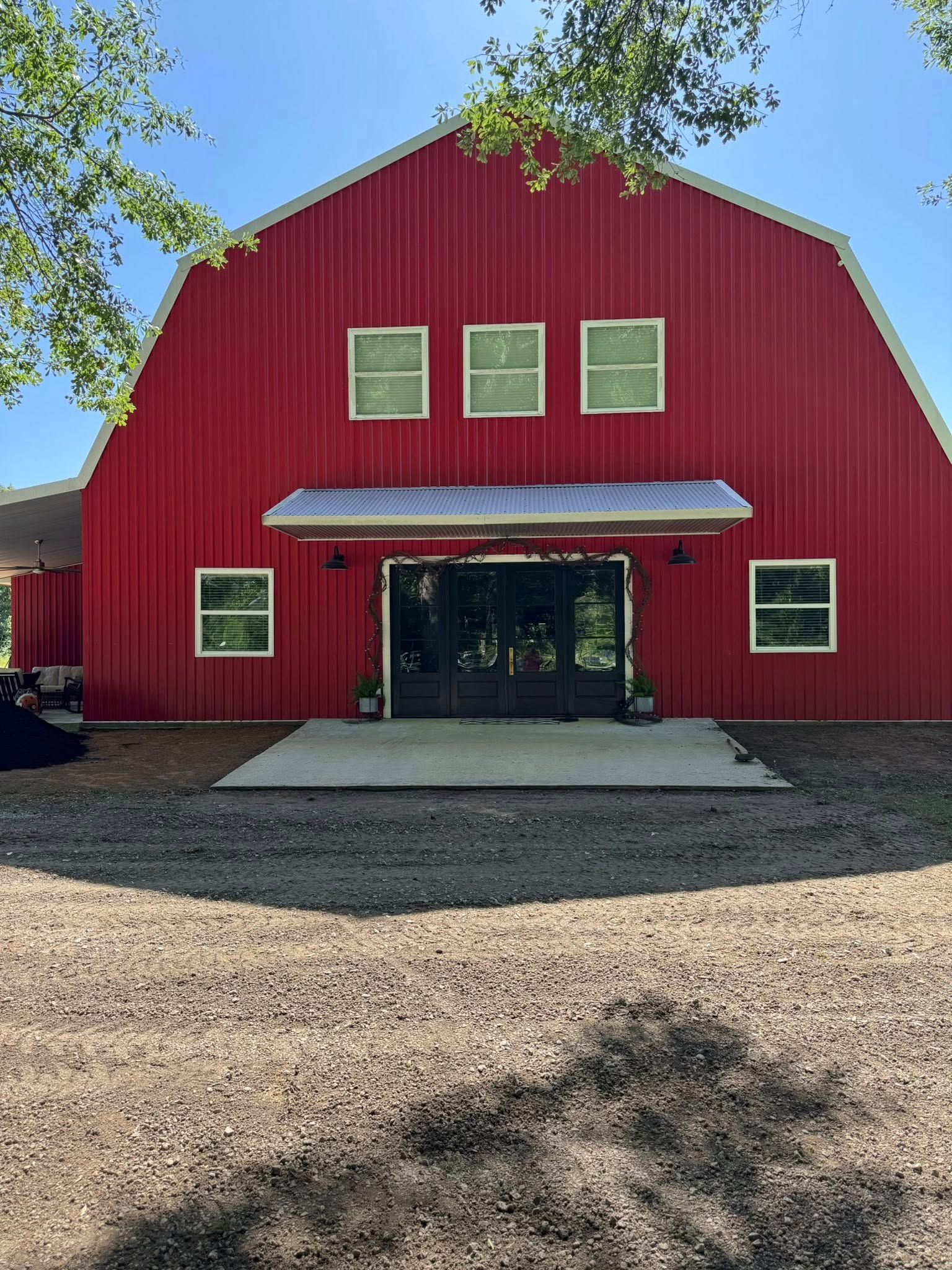 Red barn with white trim, windows, and awning. Gravel driveway.