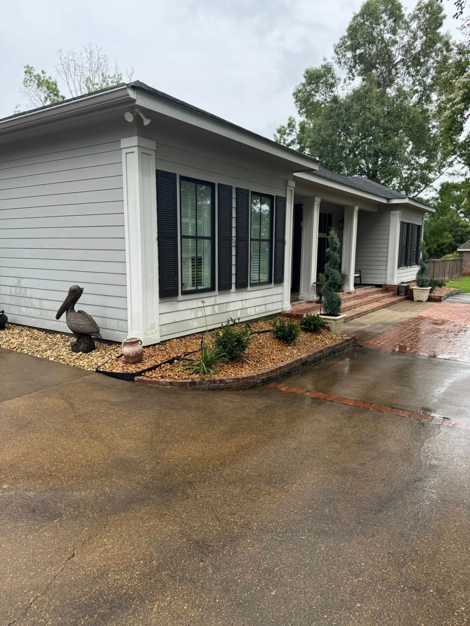 Gray house with black shutters, brick walkway, and landscaped yard.