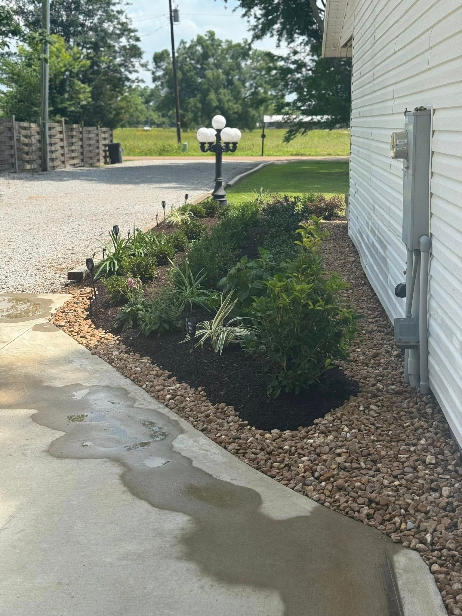 Small landscaped garden with dark rocks bordering a walkway beside a white building.