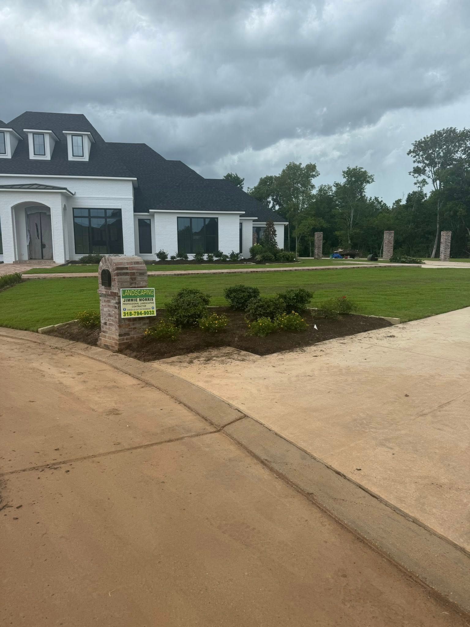 White house with dark roof and green lawn on an overcast day. Brick mailbox in the foreground.