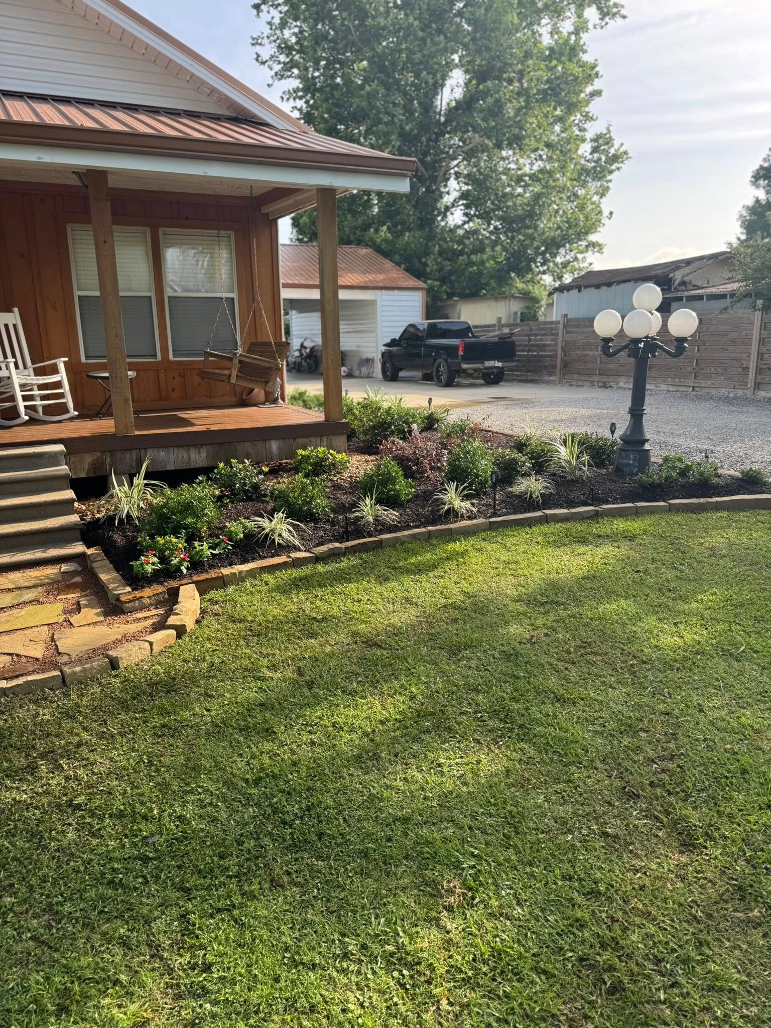 A house with a porch and flower beds in front. A black pickup truck is in the gravel driveway.