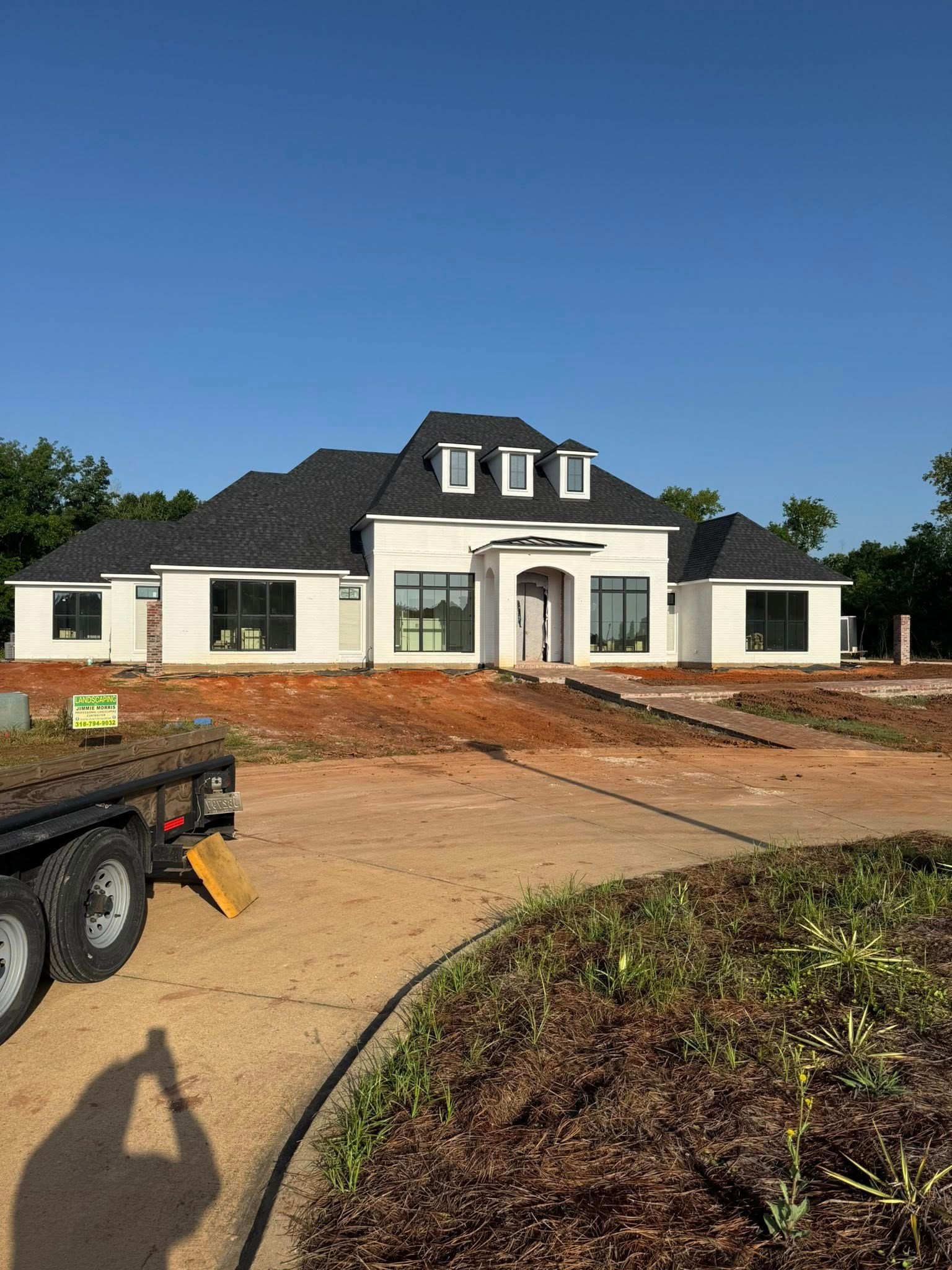 White house under construction, with black roof and windows, set in a brown dirt lot.