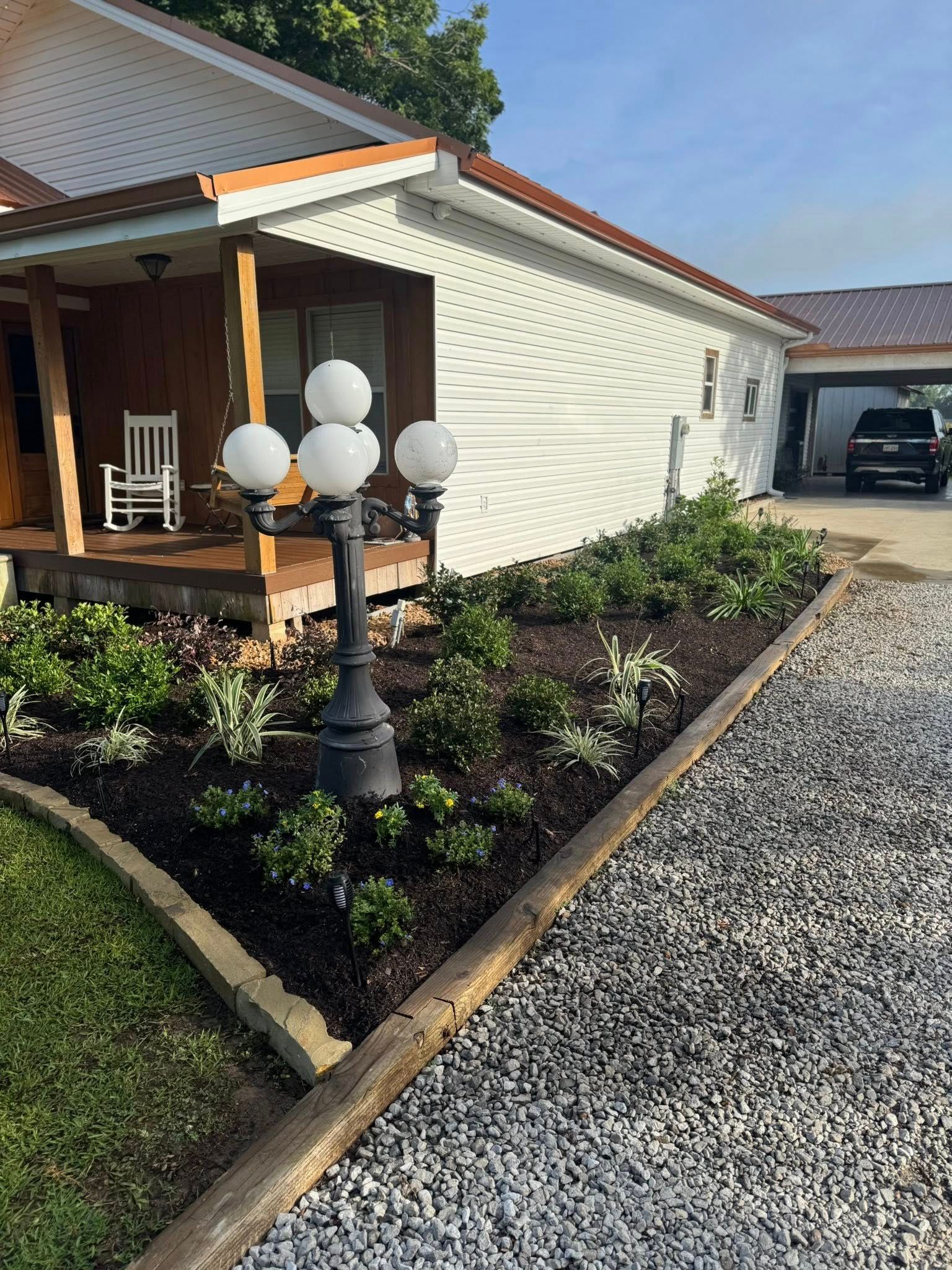 A house with a newly landscaped flower bed and a decorative lamp post in front of it.