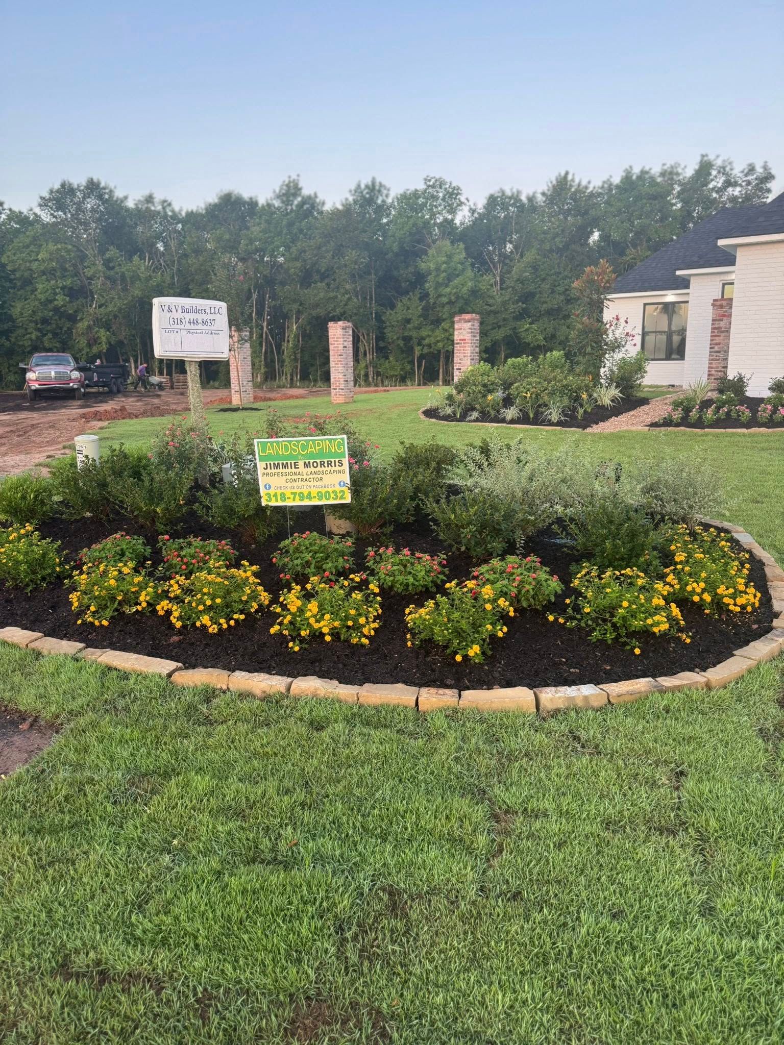 Flowerbed with yellow flowers, dark mulch, and a sign on a grassy lawn.