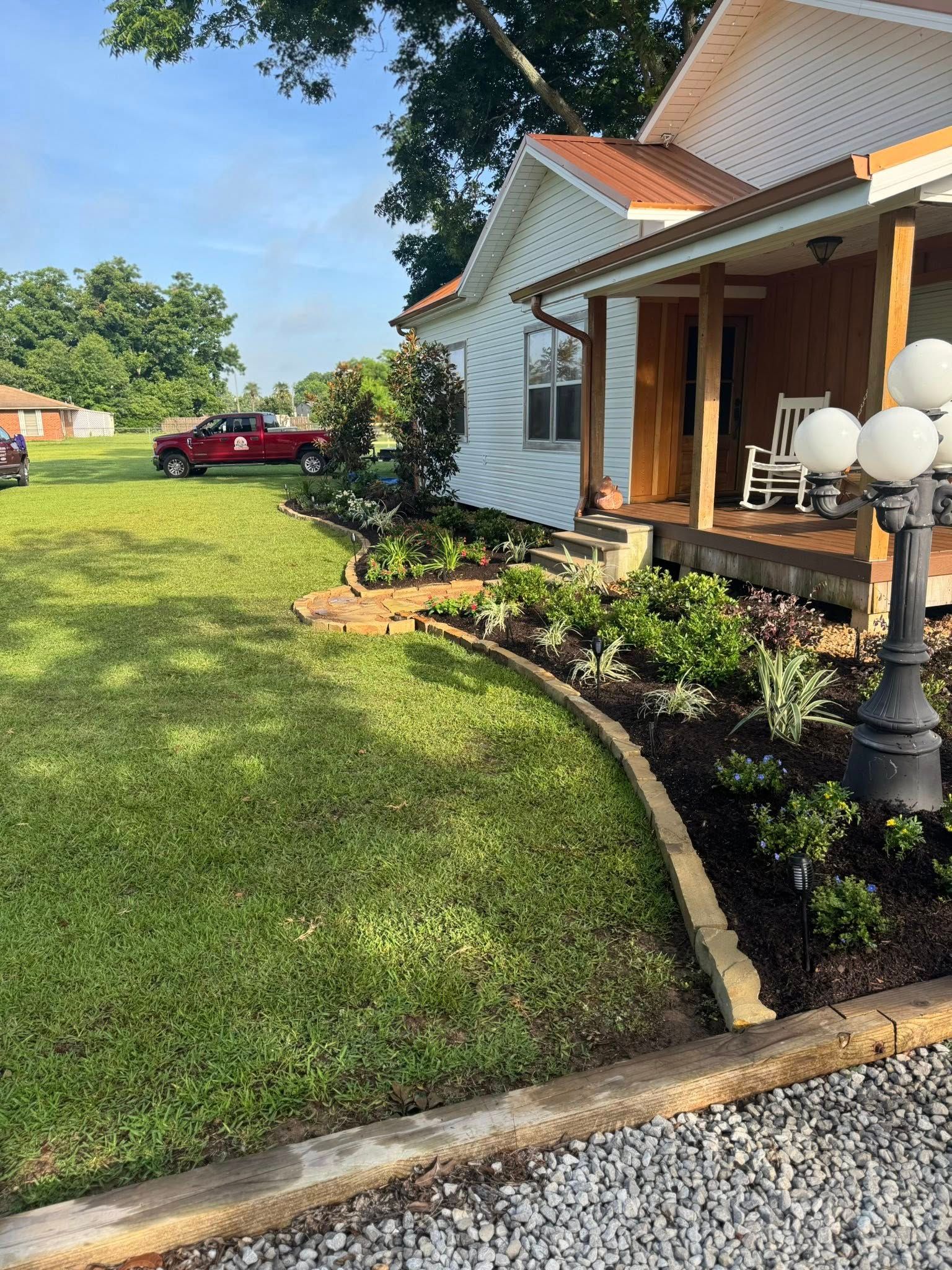 A white house with a porch and landscaping. Red truck parked on the green lawn.