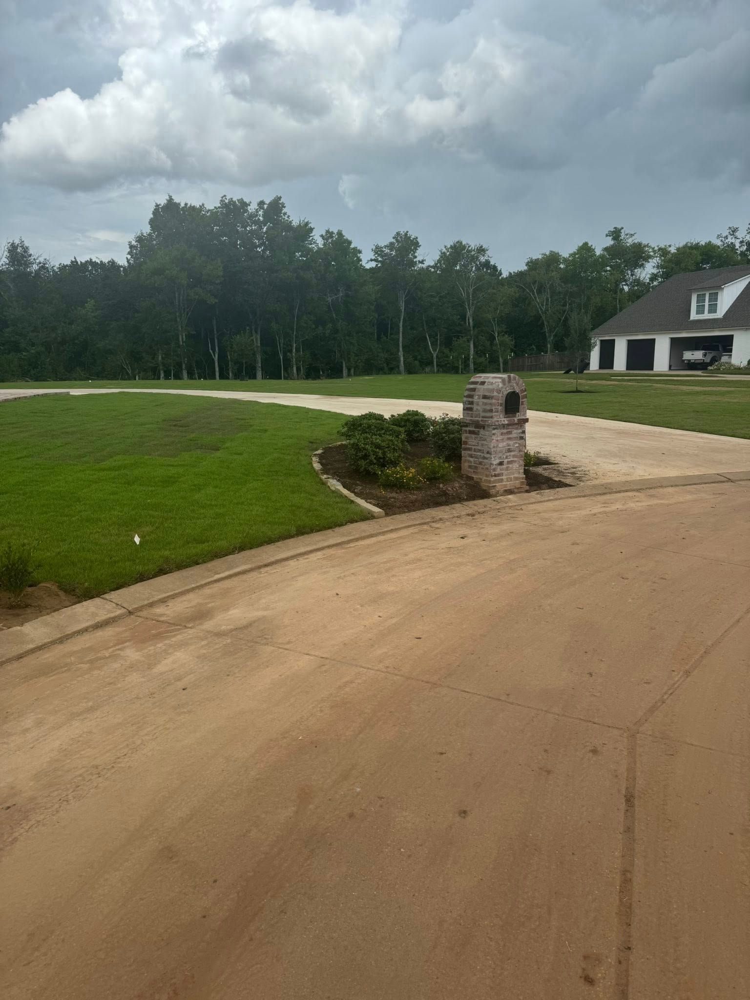 Brick mailbox in front yard with lawn and house in the background. Overcast sky.