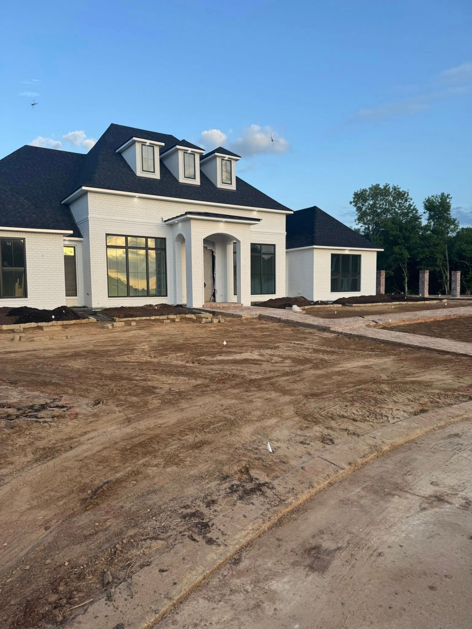 White house with black roof and windows on a dirt lot.