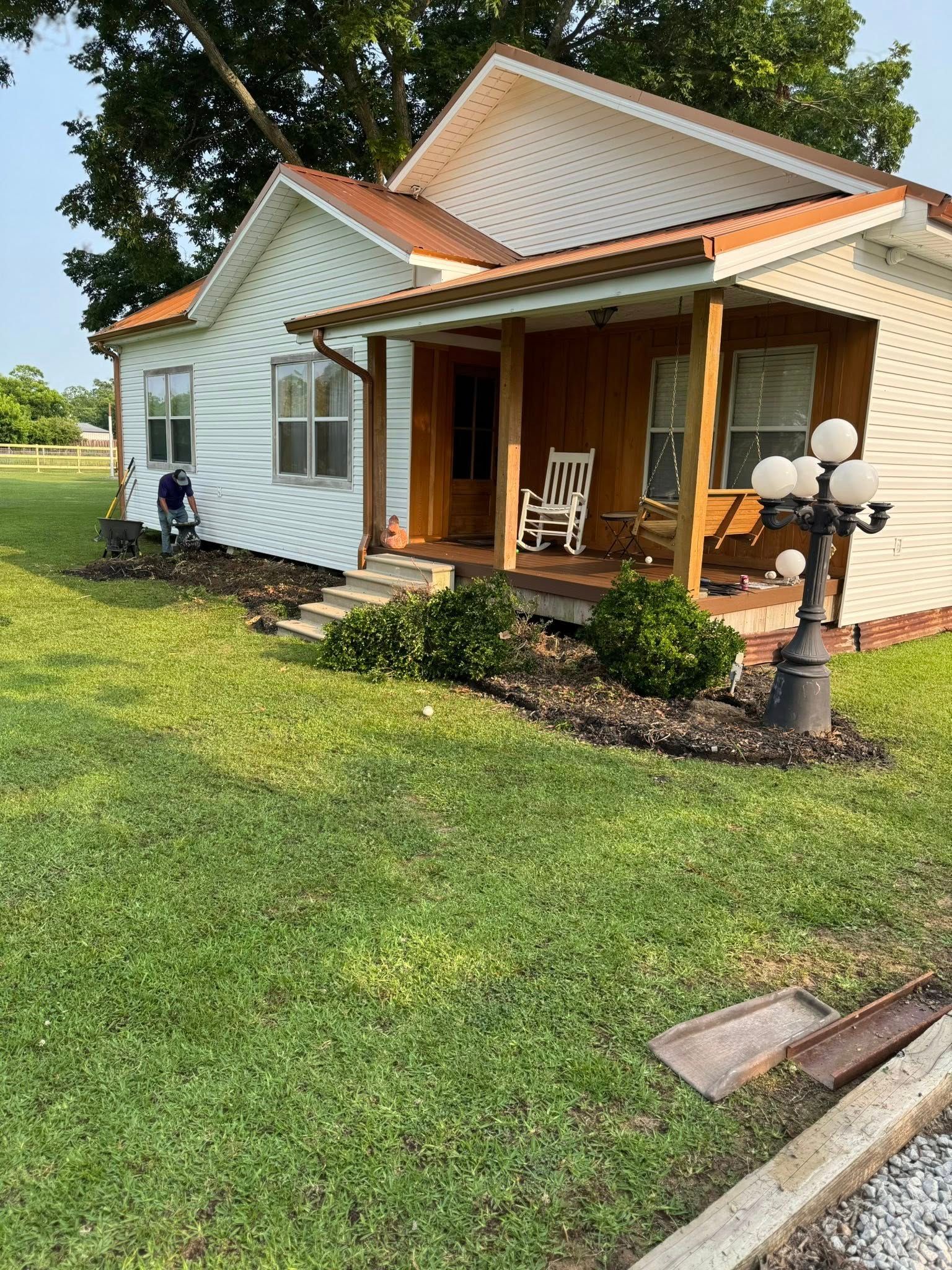 White house with brown roof and porch, rocking chair, lawn, and black lamppost.