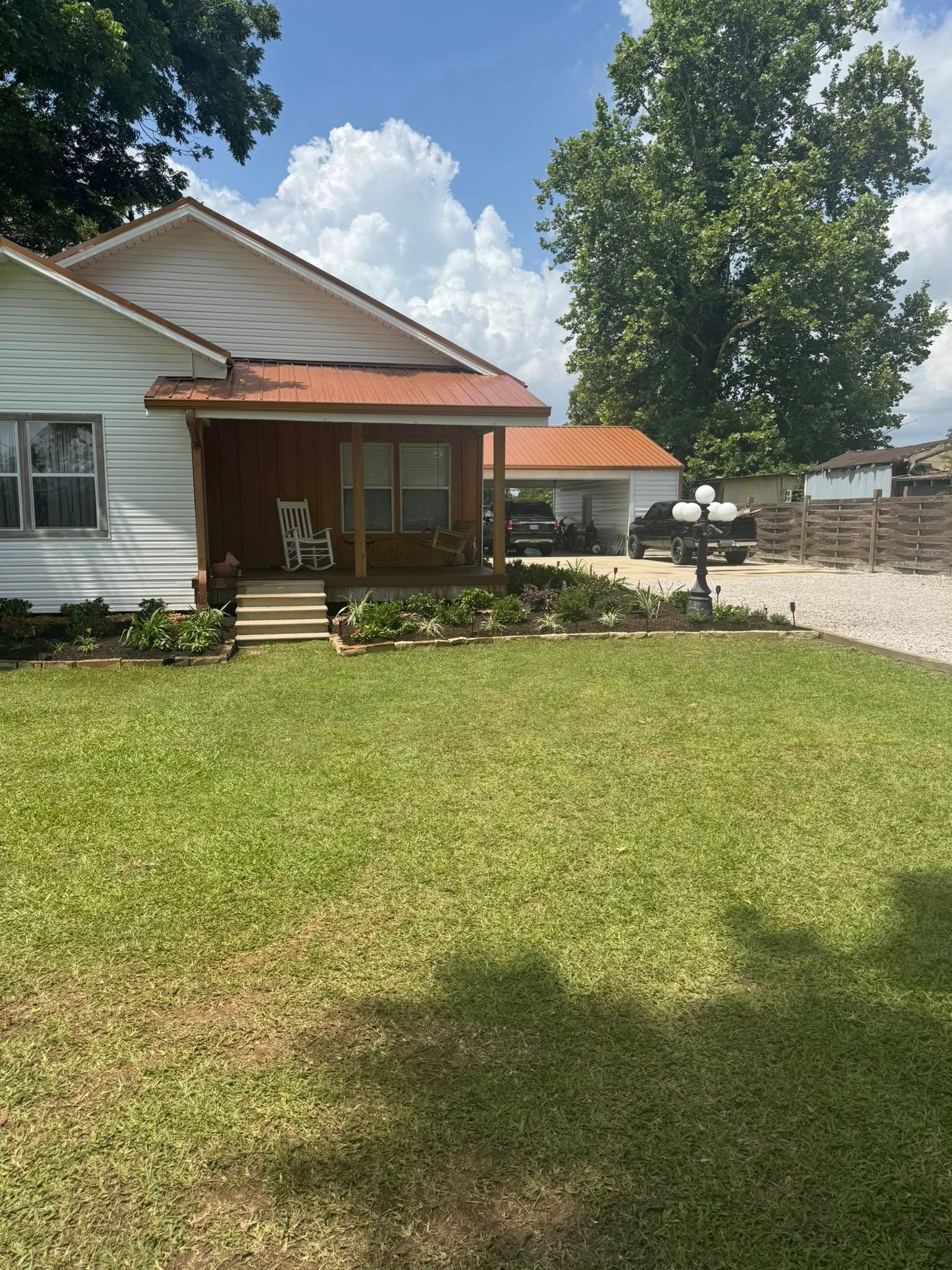 White house with a copper-colored roof and porch, on a green lawn with a tree and driveway.