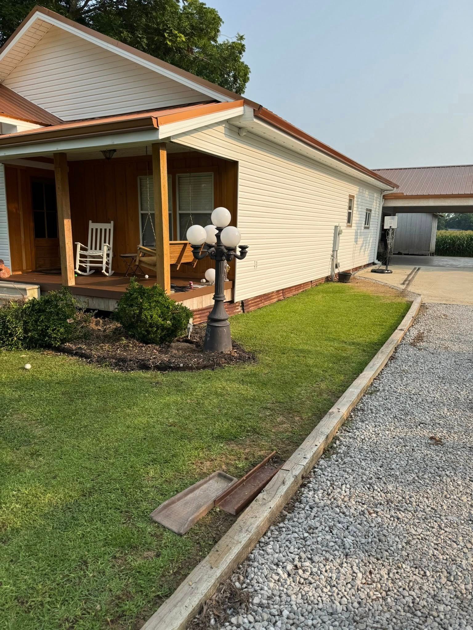 A small house with white siding and brown trim. A porch with a rocking chair and a lamp post are in the front yard.
