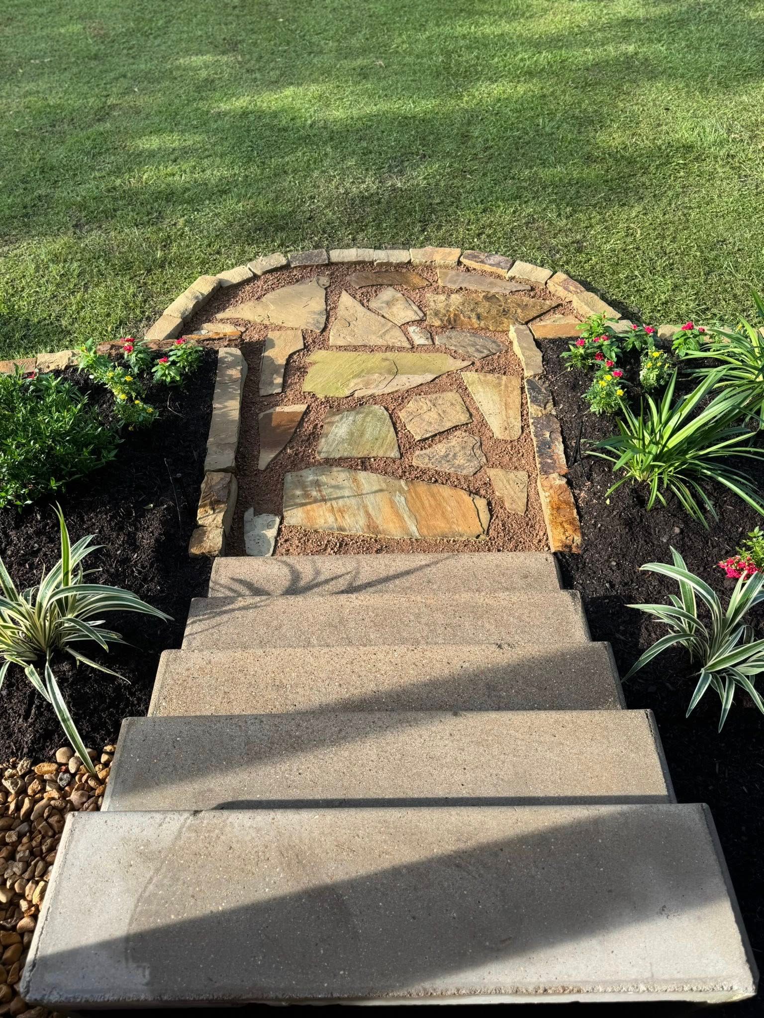 Stone steps leading up to a flagstone pathway surrounded by flowerbeds and grass.