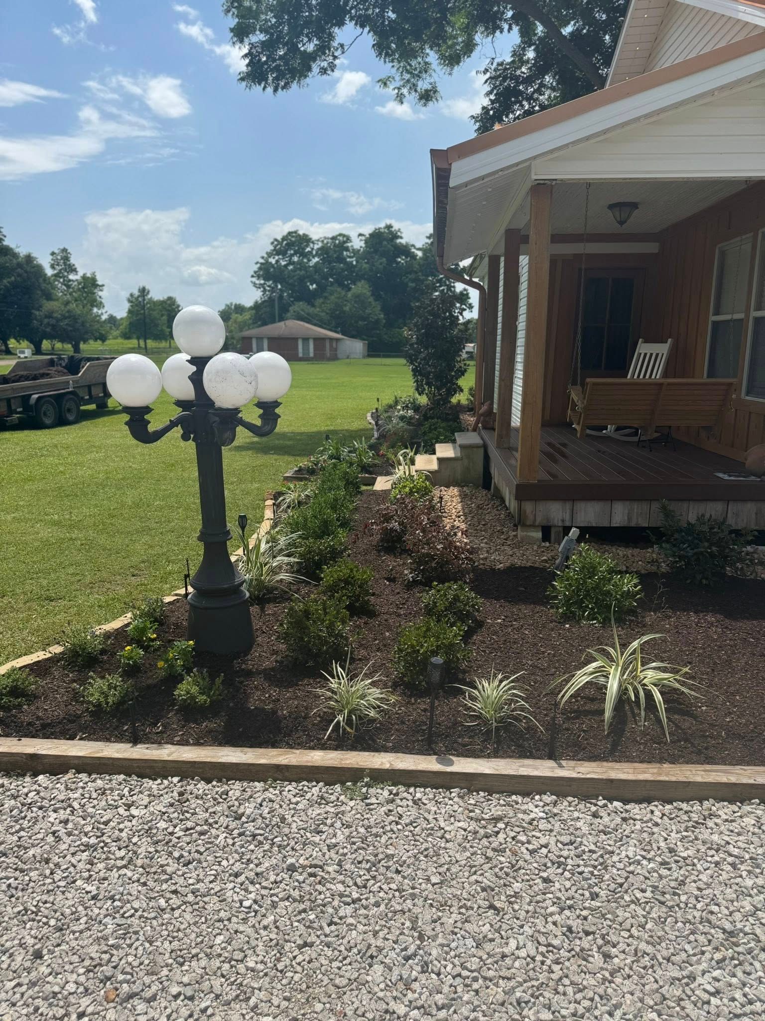 A house with a porch, landscaping, and a multi-globe lamp post on a gravel driveway.