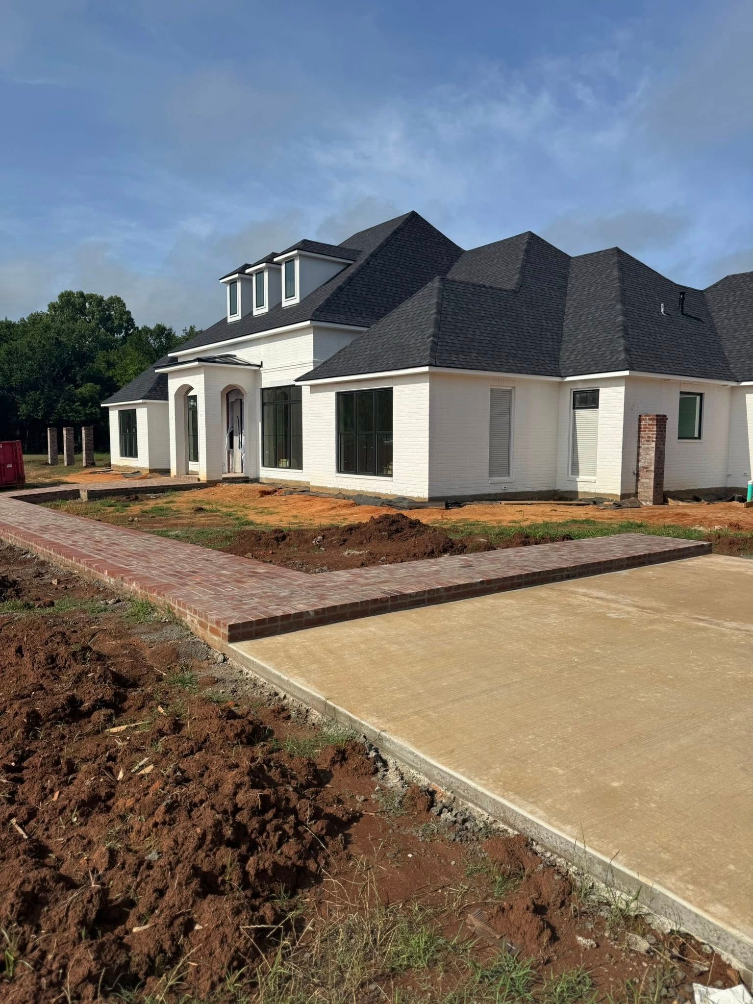 White house under construction with brick pathway and driveway.