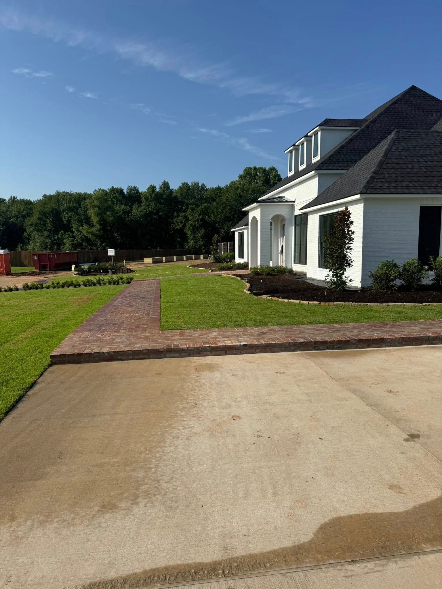 White house with dark roof, brick walkway, and green lawn under a blue sky.