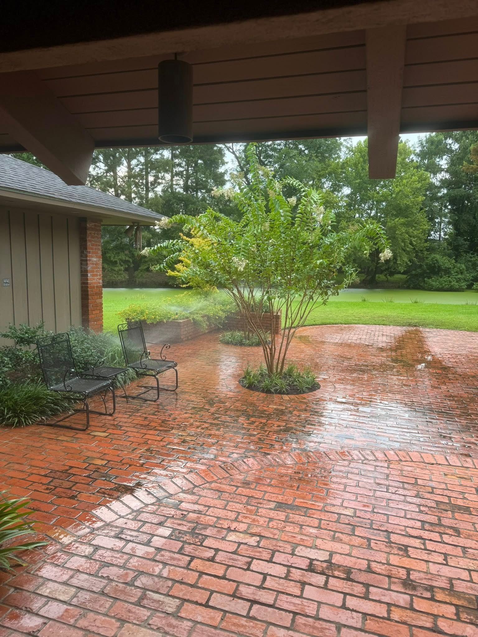 Brick patio with water, a small tree, and a bench under a covered porch.