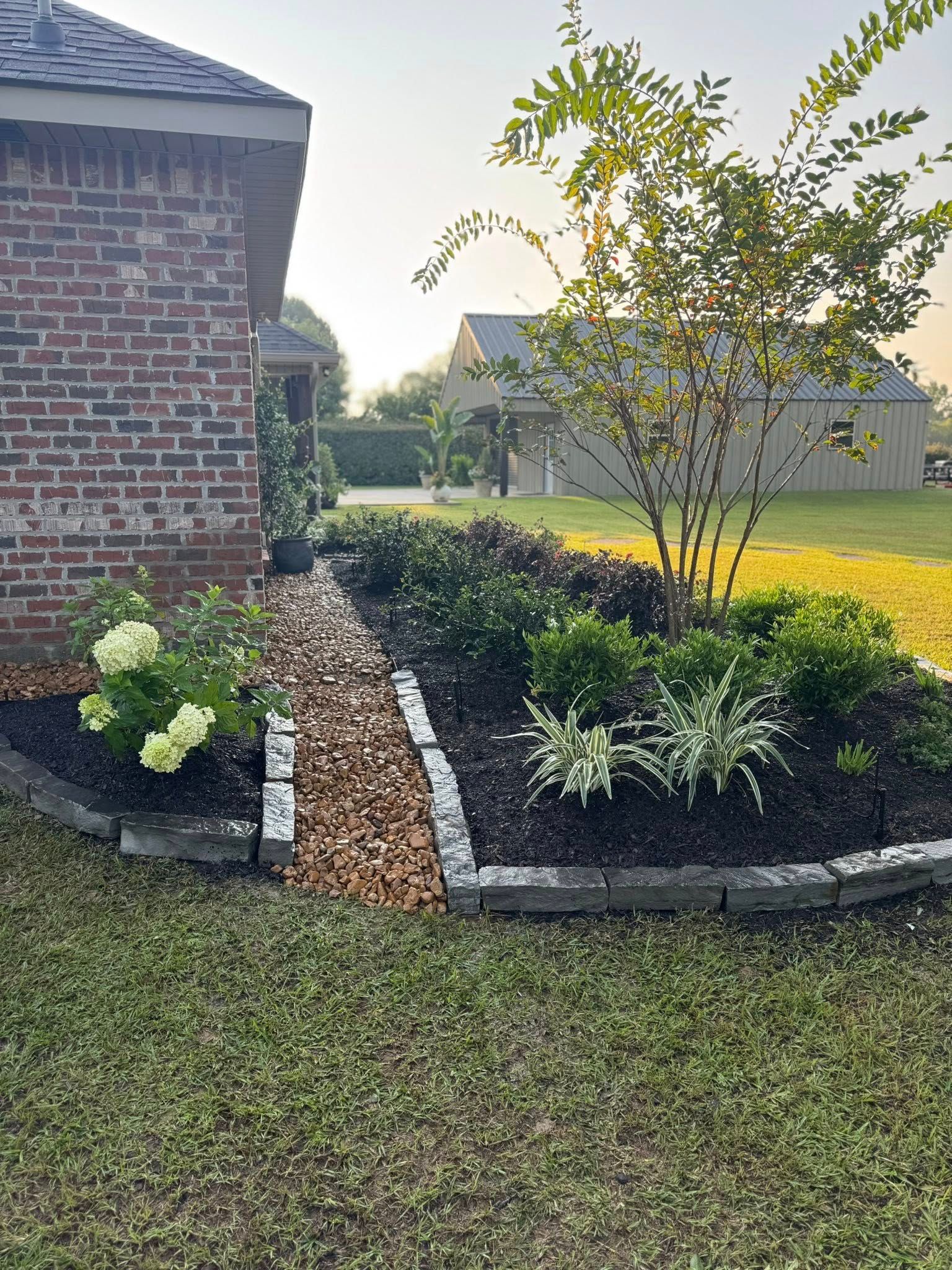Landscaped garden bed with dark mulch and stone edging, next to brick home.