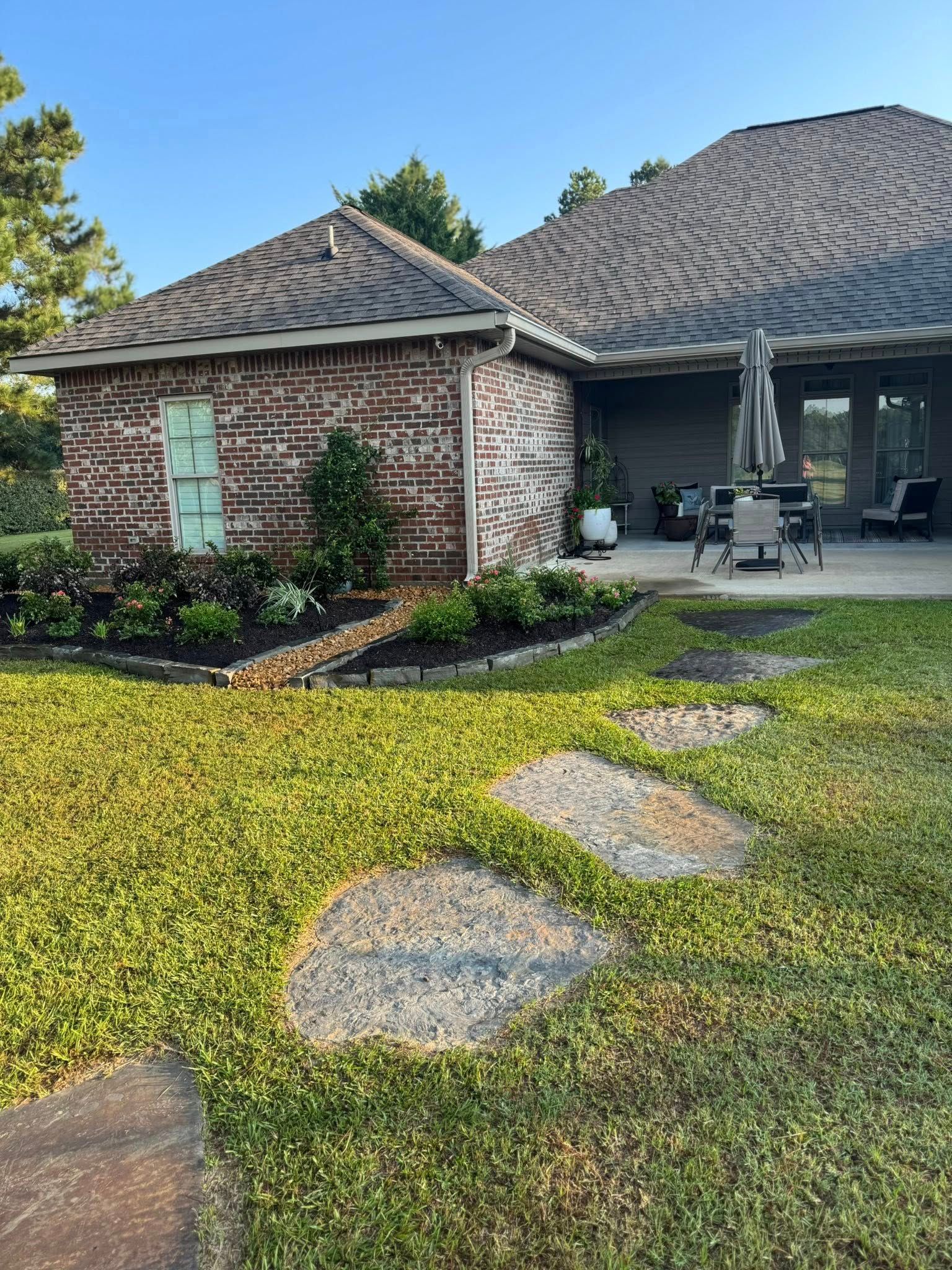Brick building with green door, patio, and stepping stones in a grassy yard.