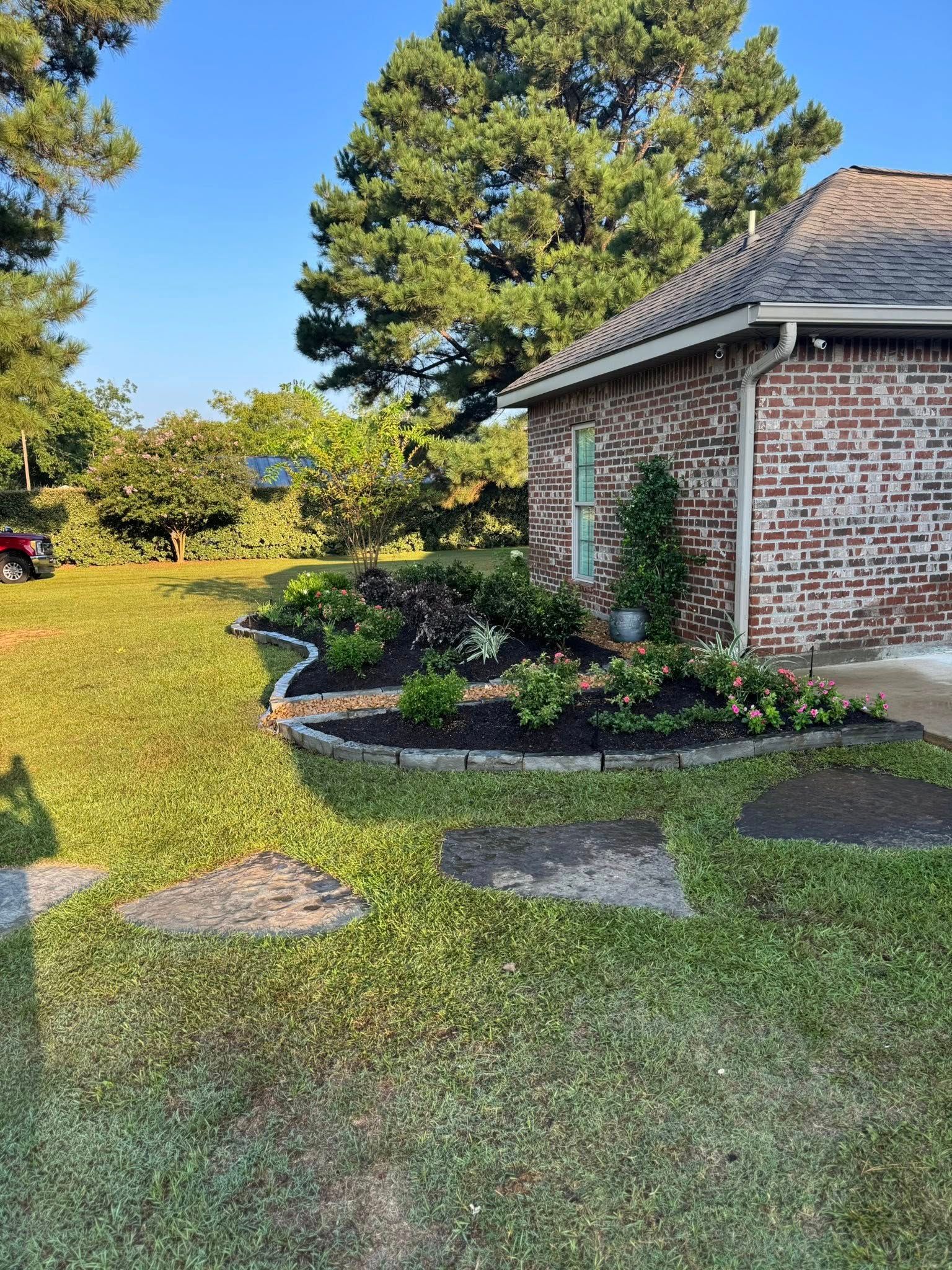 A brick house with a landscaped garden bed against a lawn. Green grass and trees are in the background.