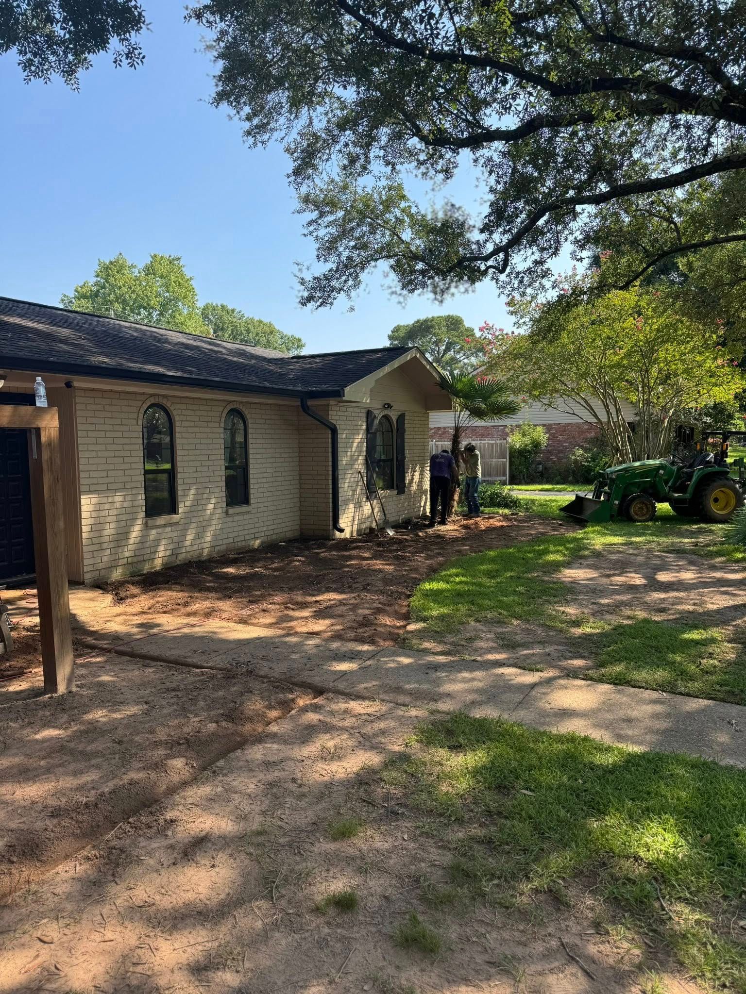 Side view of house, dirt yard, person working, and a John Deere tractor.