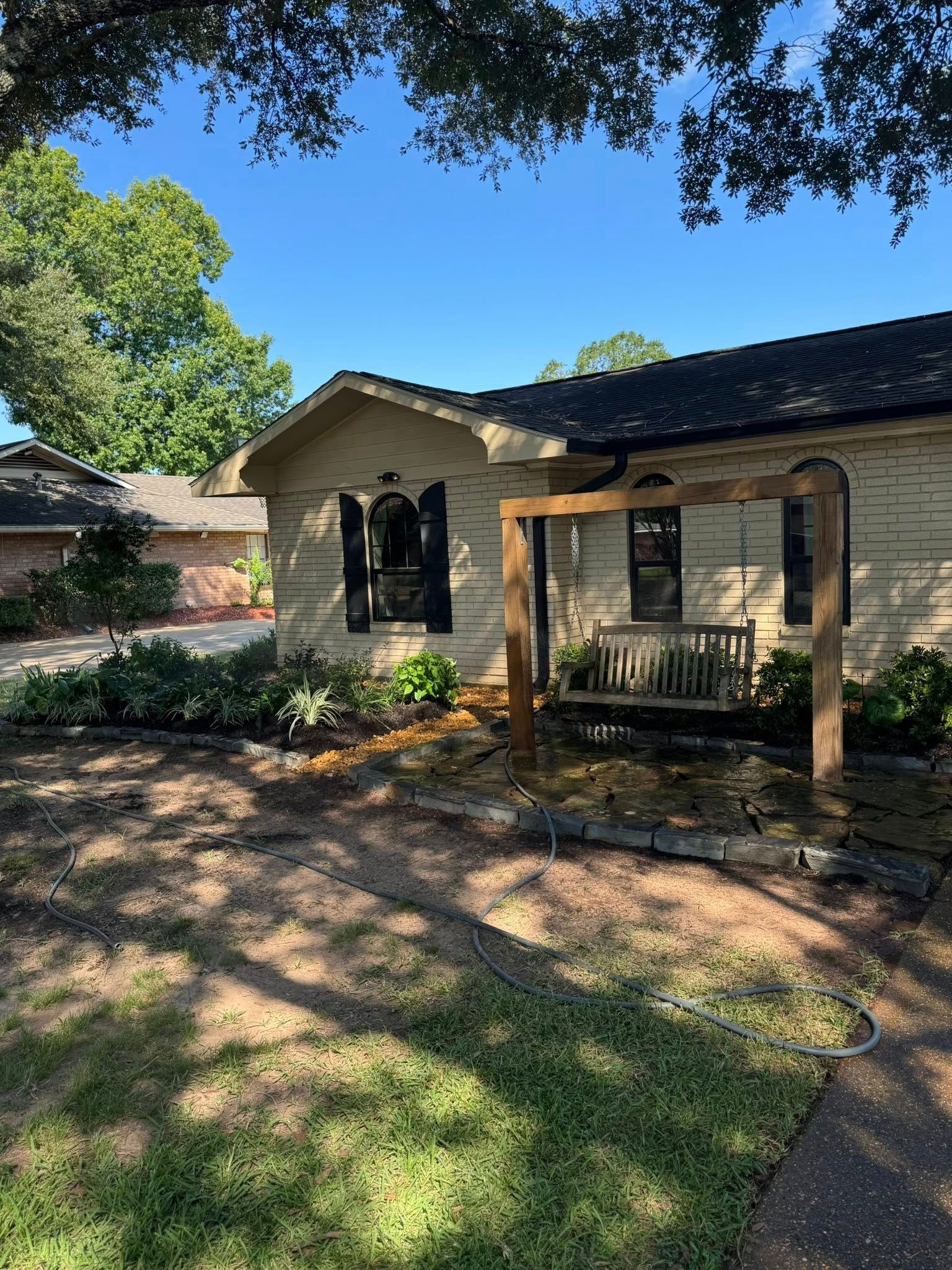 Stone-façade house with a wooden swing. Green bushes and trees surround the house on a sunny day.