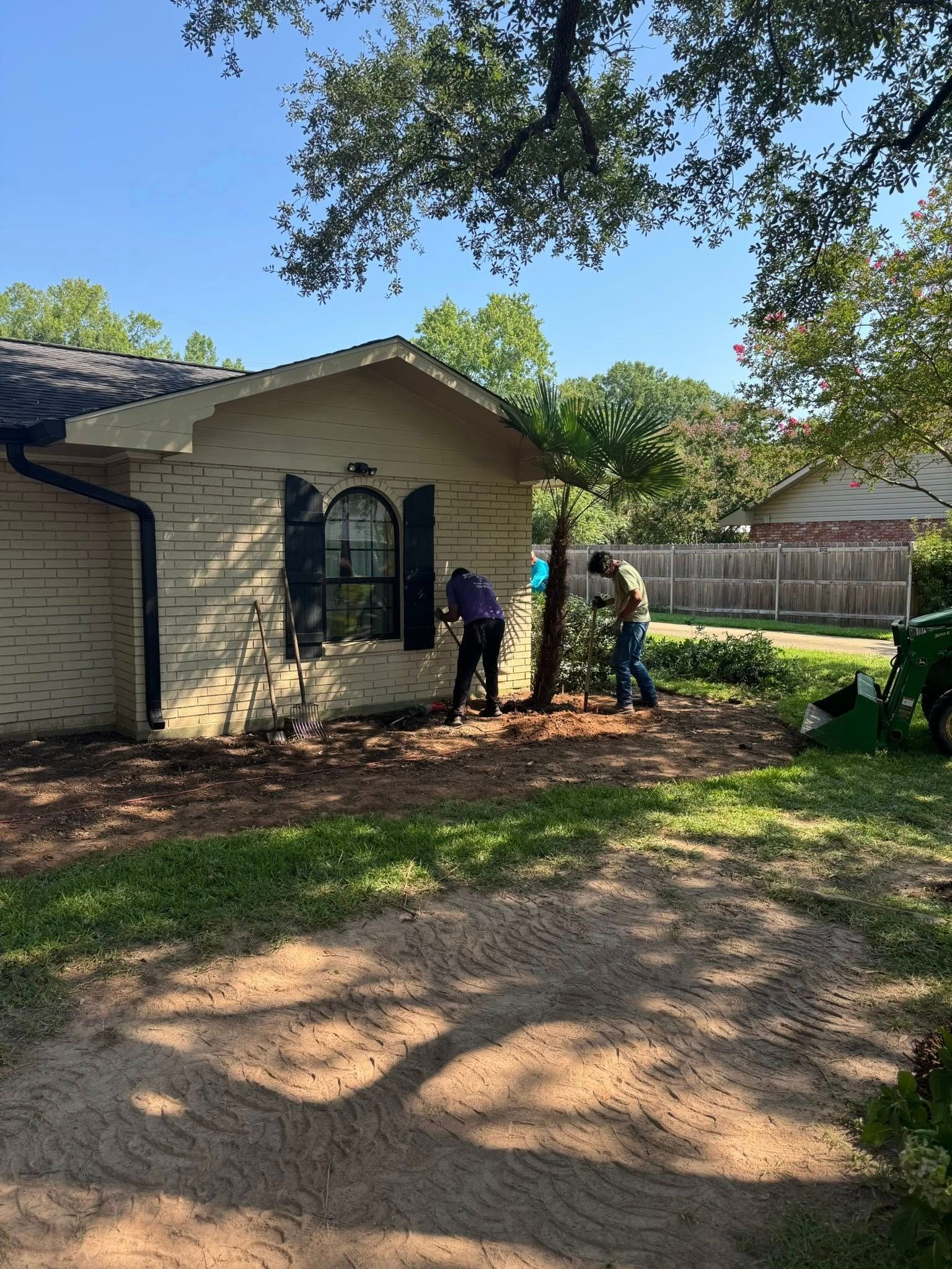 Two people removing a tree near a house. One is cutting, another collecting debris.