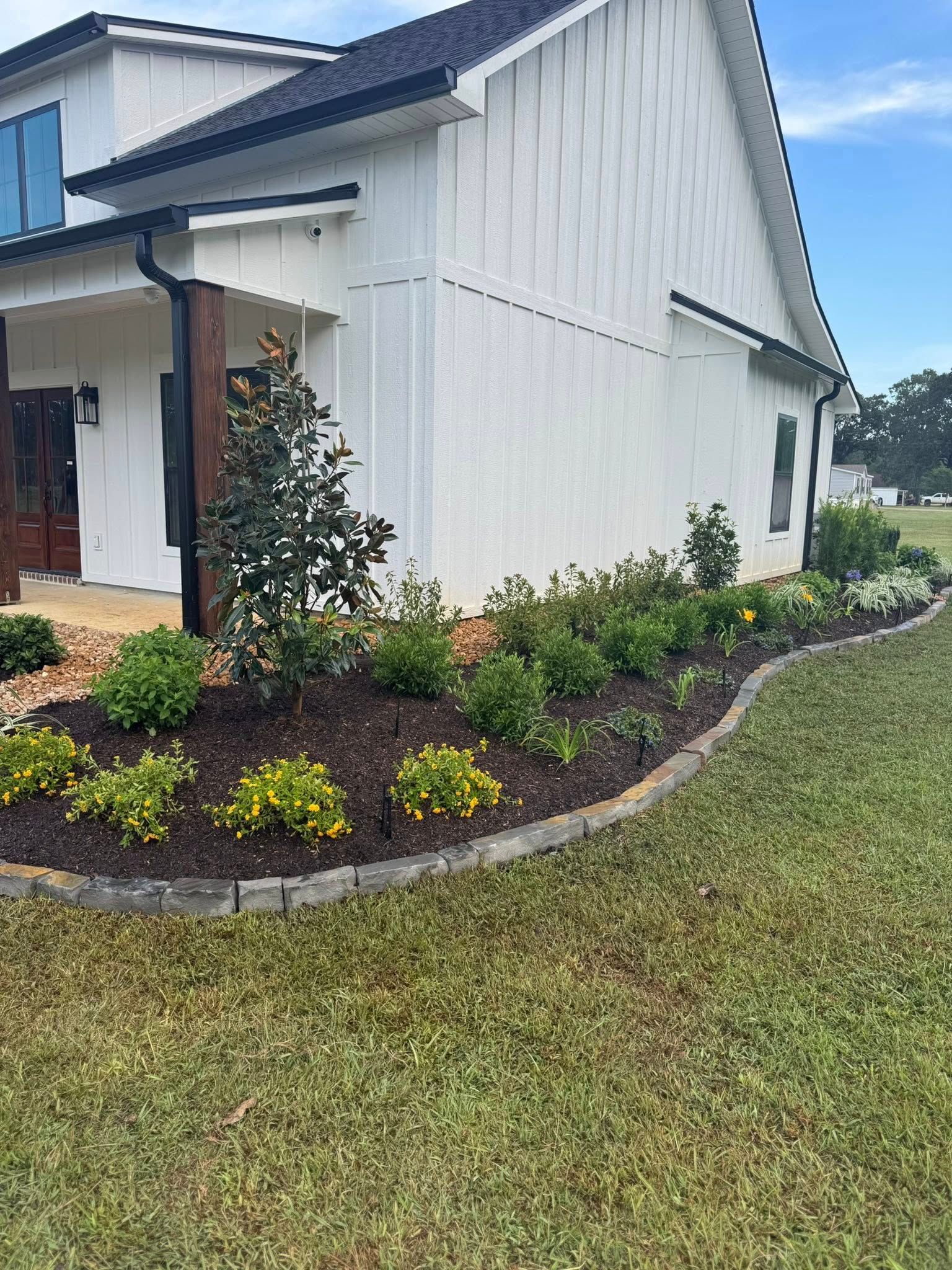 White house with a garden bed lined with stone. Lawn in foreground, blue sky in background.