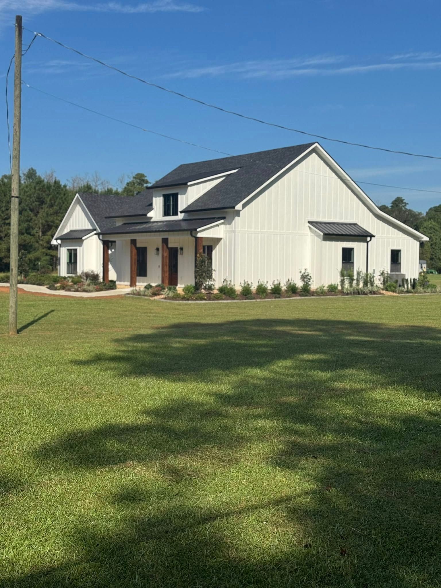 White farmhouse with black roof against a blue sky, standing in a green field.