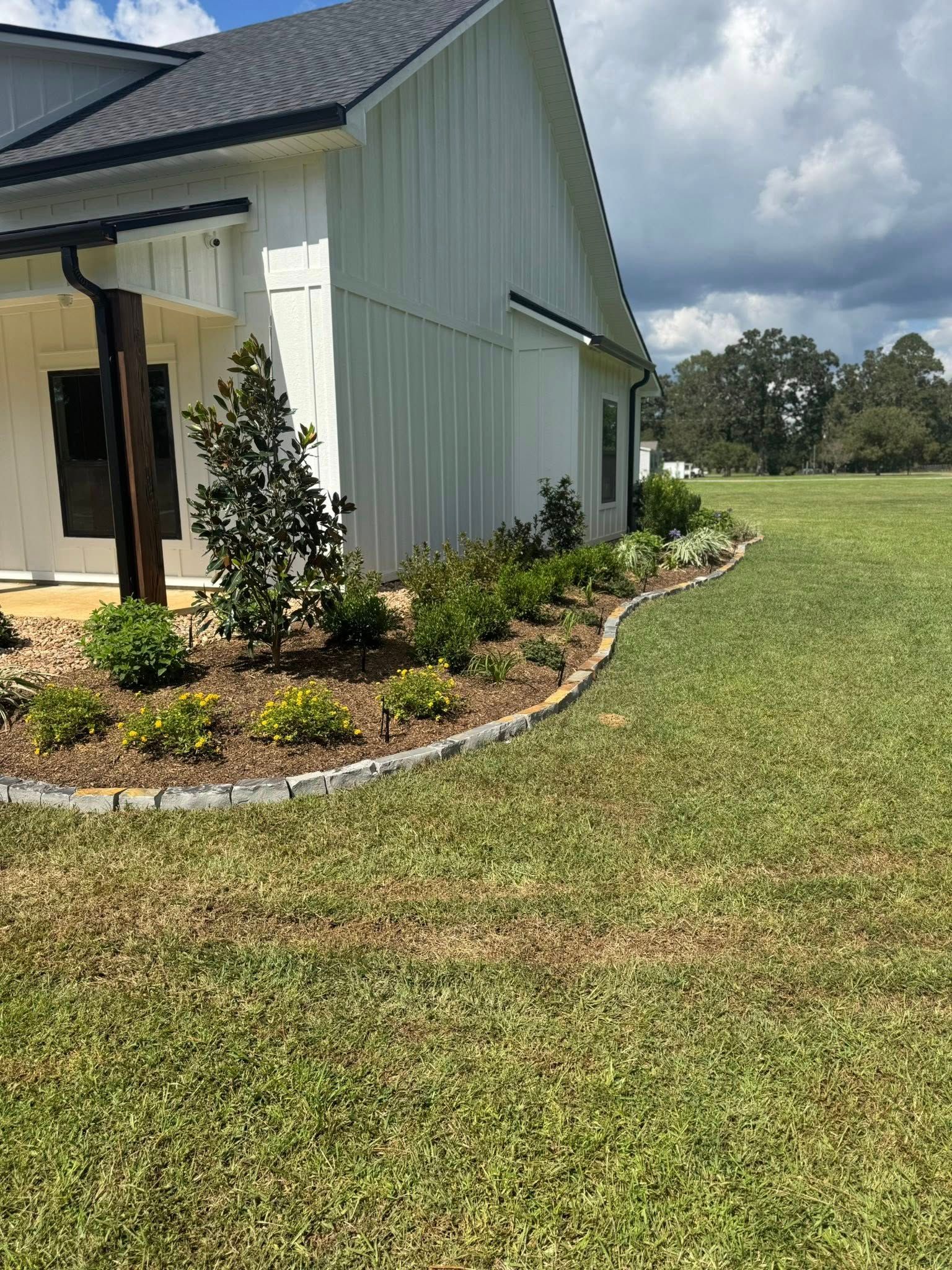 White house with landscaped flower bed and green lawn.