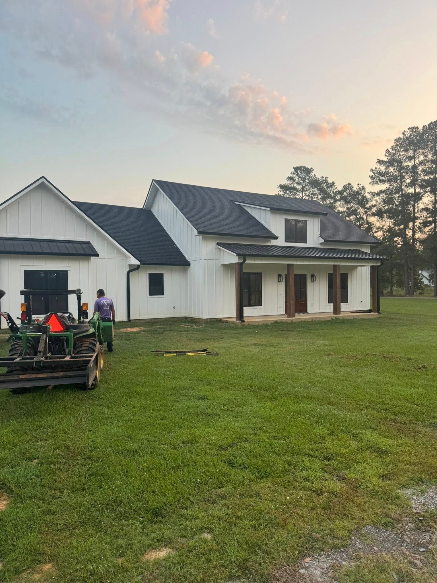 White house with black roof, brown porch columns, and a tractor on the green lawn.