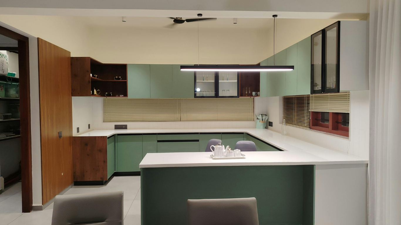 Modern U-shaped kitchen with sage green cabinets, white countertops, a central island, and wood-toned accent shelving.