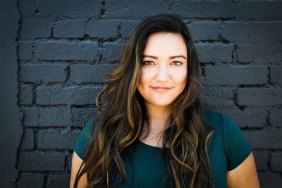 A woman with long hair is standing in front of a brick wall.