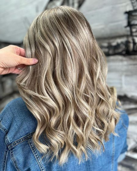 A Woman With Wavy Blonde Hair Is Getting Her Hair Done In A Salon — Genesis Hair and Beauty In Port Kembla, NSW