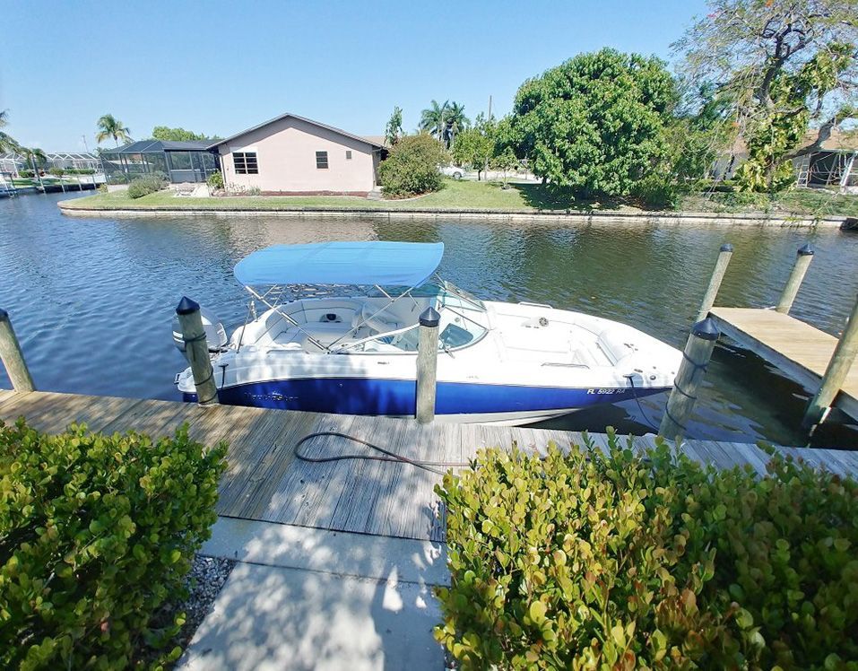White and blue motorboat docked by a canal with green shrubs and houses across the water