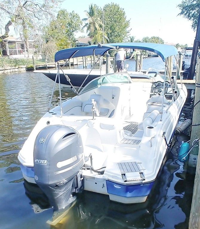 White motorboat docked on calm water beside a canal and trees, with a covered seating area and outboard motor