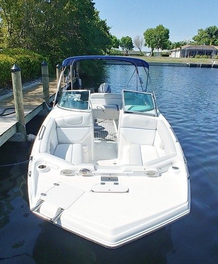 White speedboat docked on calm water beside a canal, with white seats and a blue canopy.