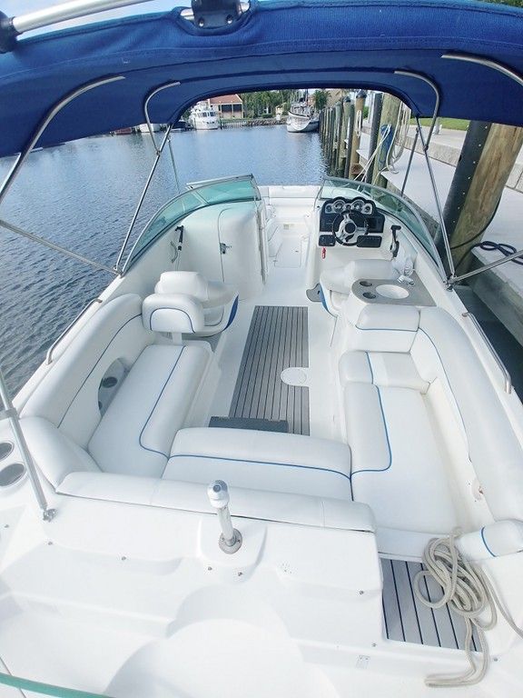White-cushioned boat cockpit with canopy, helm, seating, and a view of water and docks ahead