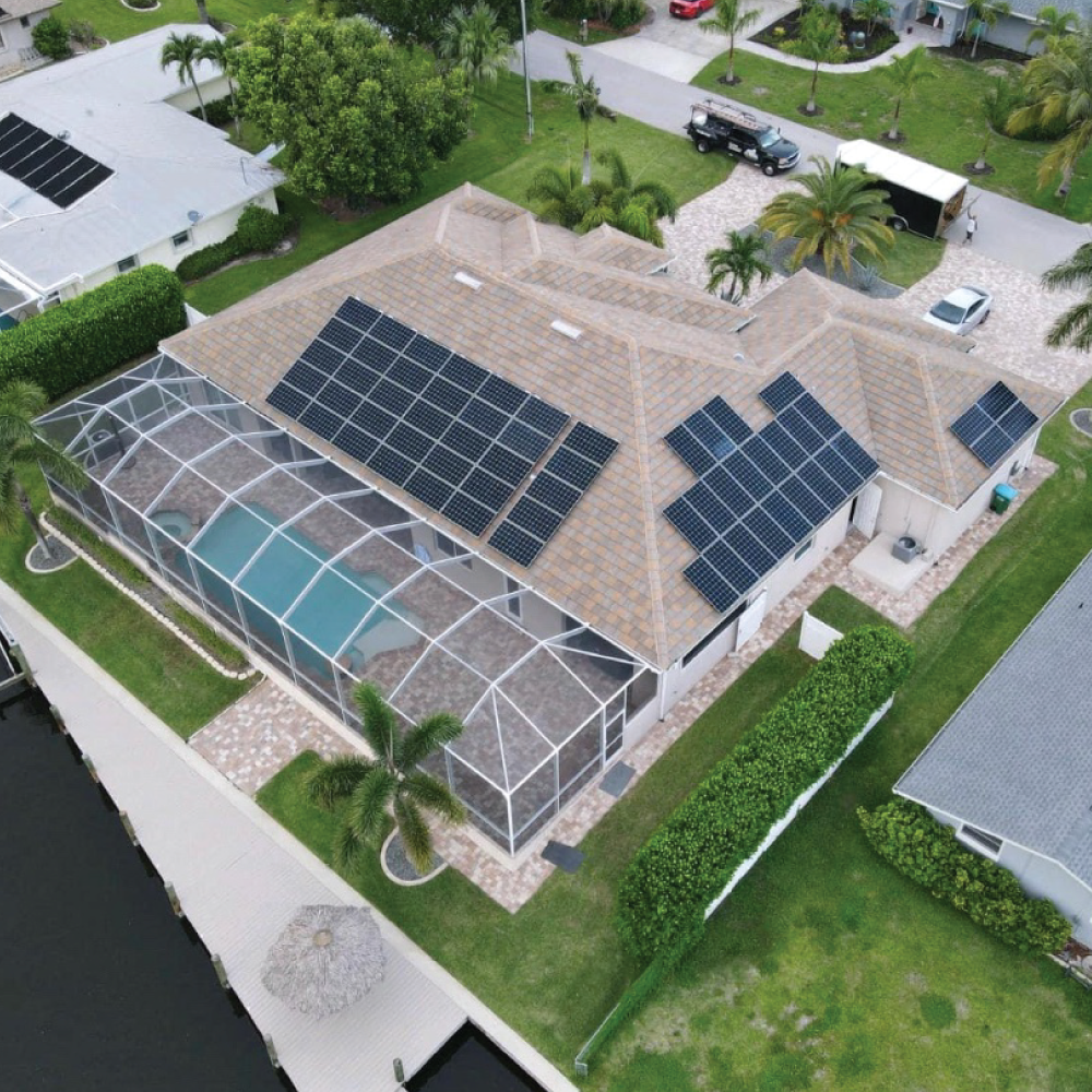 Aerial view of a house with dark solar panels, a screened pool enclosure, and a green lawn.