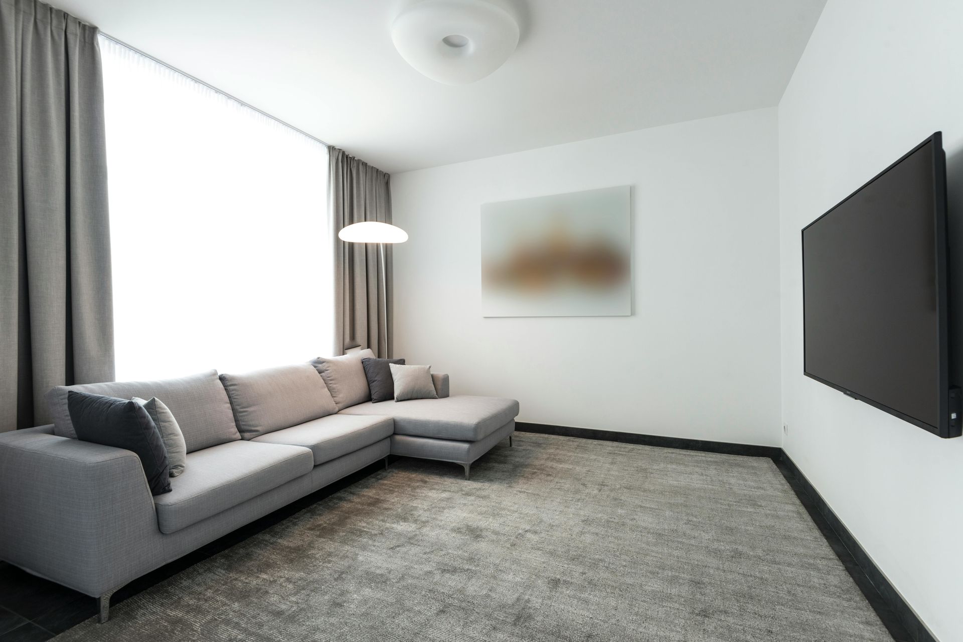 A modern meeting room features a concrete-style table, black chairs, orange accents, and a wall-mounted TV.