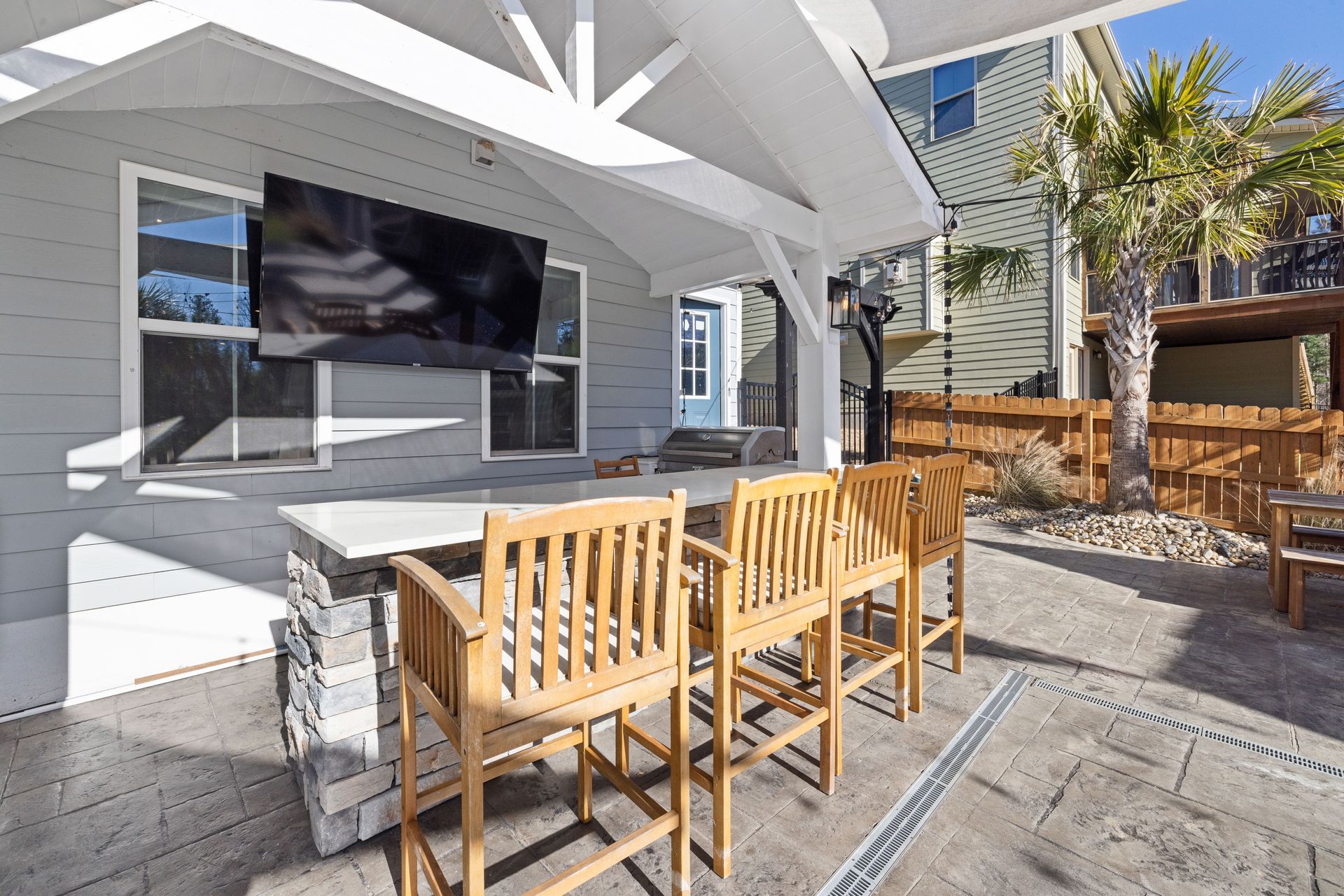 Outdoor patio with wooden chairs, tables, and a shaded seating area beside a modern house