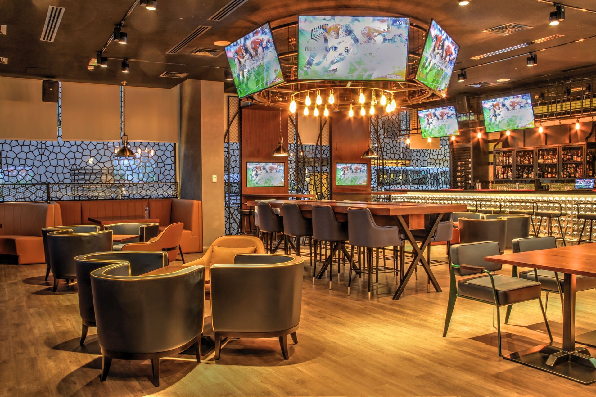 Empty modern bar interior with TVs, warm lighting, and tables and chairs arranged for customers