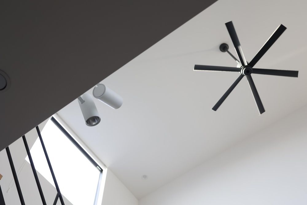 Modern white ceiling with black ceiling fan and track lights, viewed from below by a staircase.