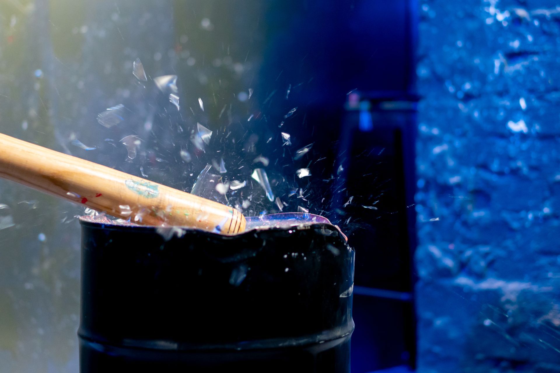 Baseball bat shatters a black barrel, shards of debris flying, bright light.