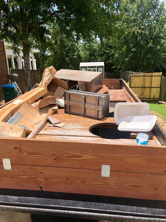 Wooden dumpster filled with cardboard boxes, a white foam container, and debris in a yard.