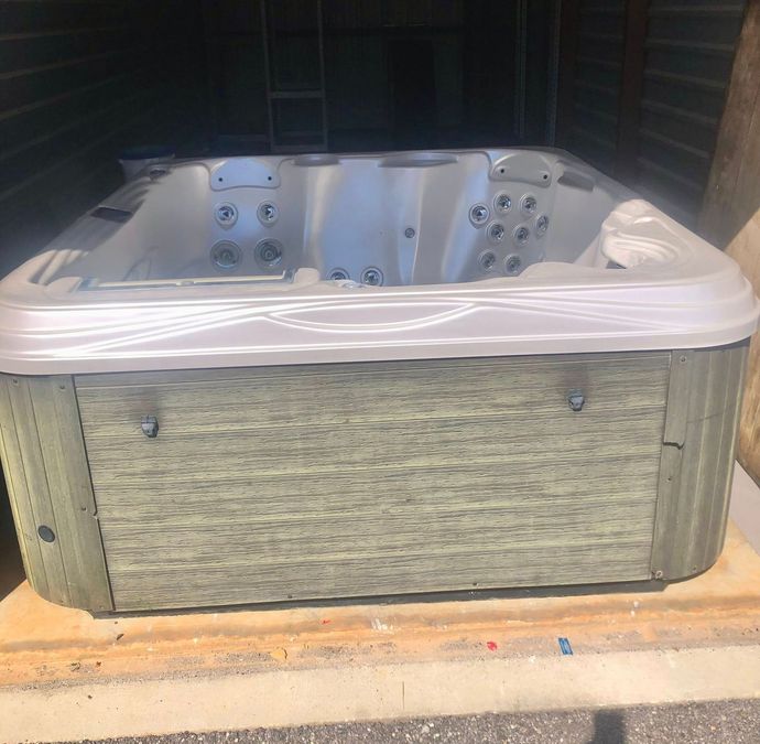 Large gray outdoor hot tub with a white cover, shown in a shed or garage.