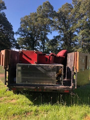 Overturned red vehicle in grass, with damaged front and exposed radiator, trees in background