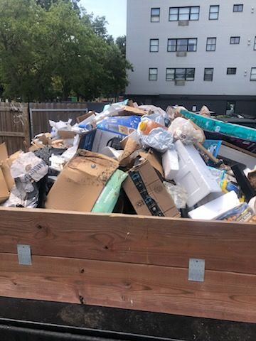 Overflowing dumpster filled with mixed trash and cardboard outdoors beside an apartment building