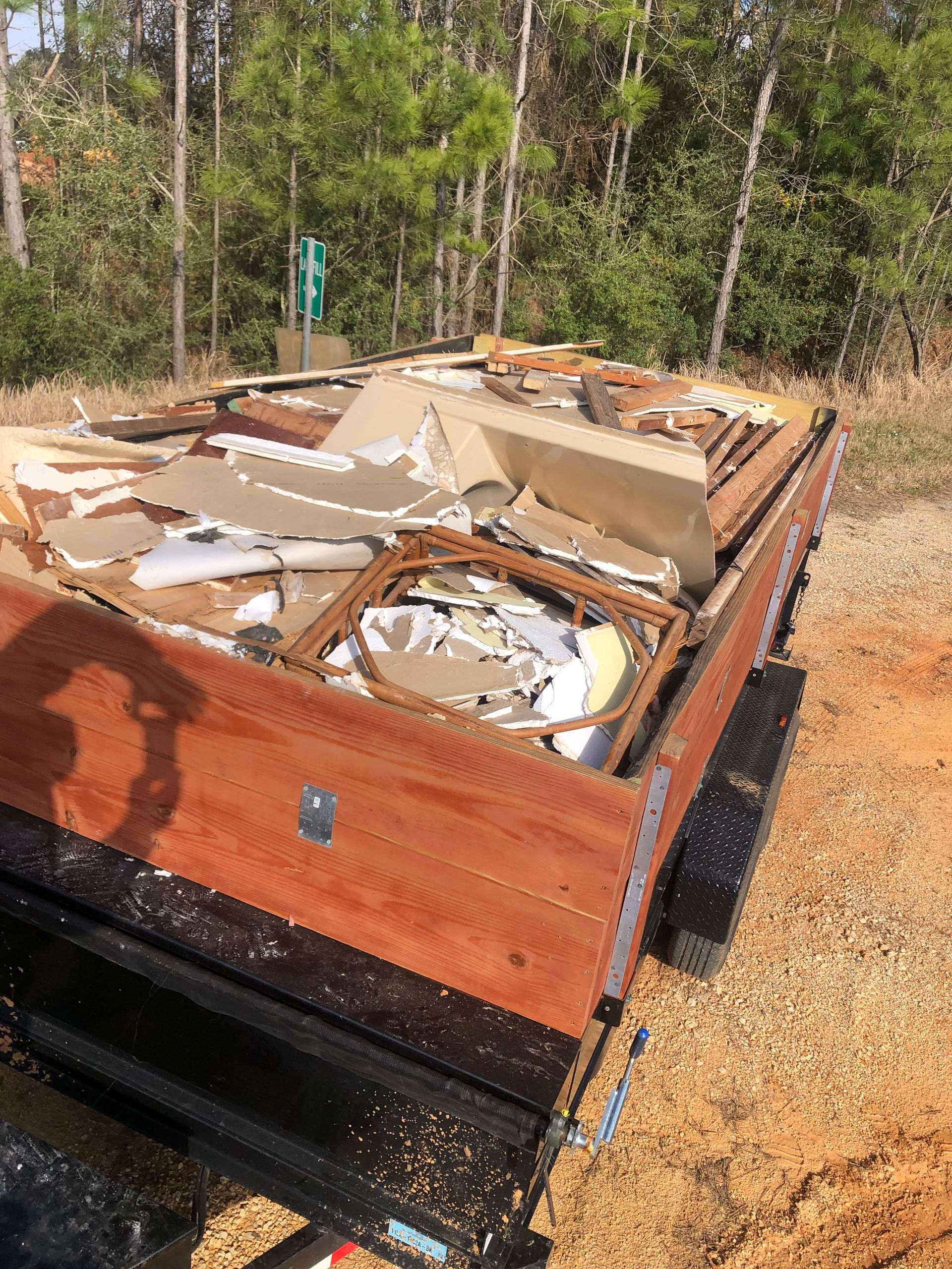 Damaged wooden trailer or box in a wooded area, filled with broken debris and metal scraps.