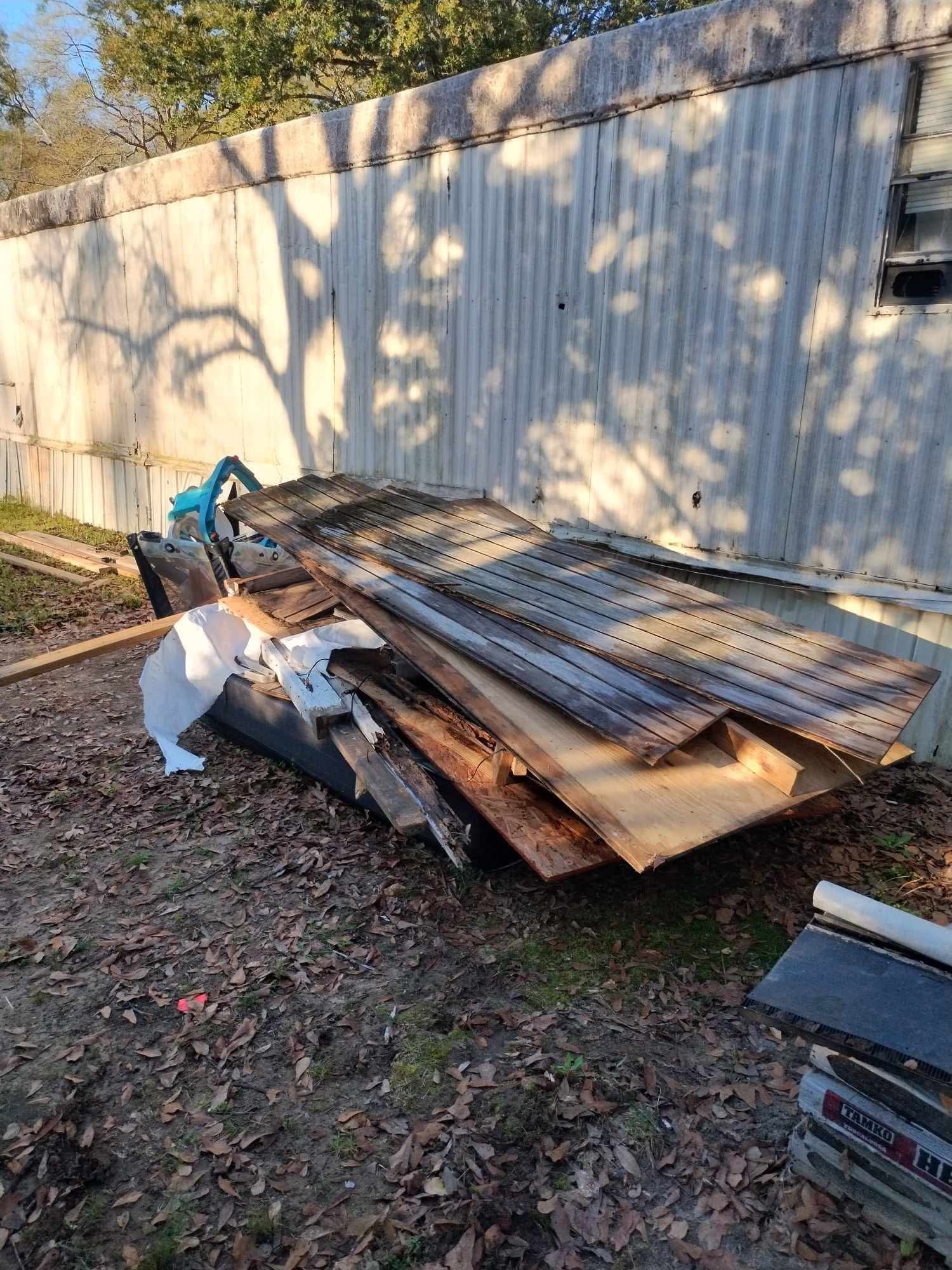 Pile of scrap wood and metal pallets beside a white fence in a sunlit yard