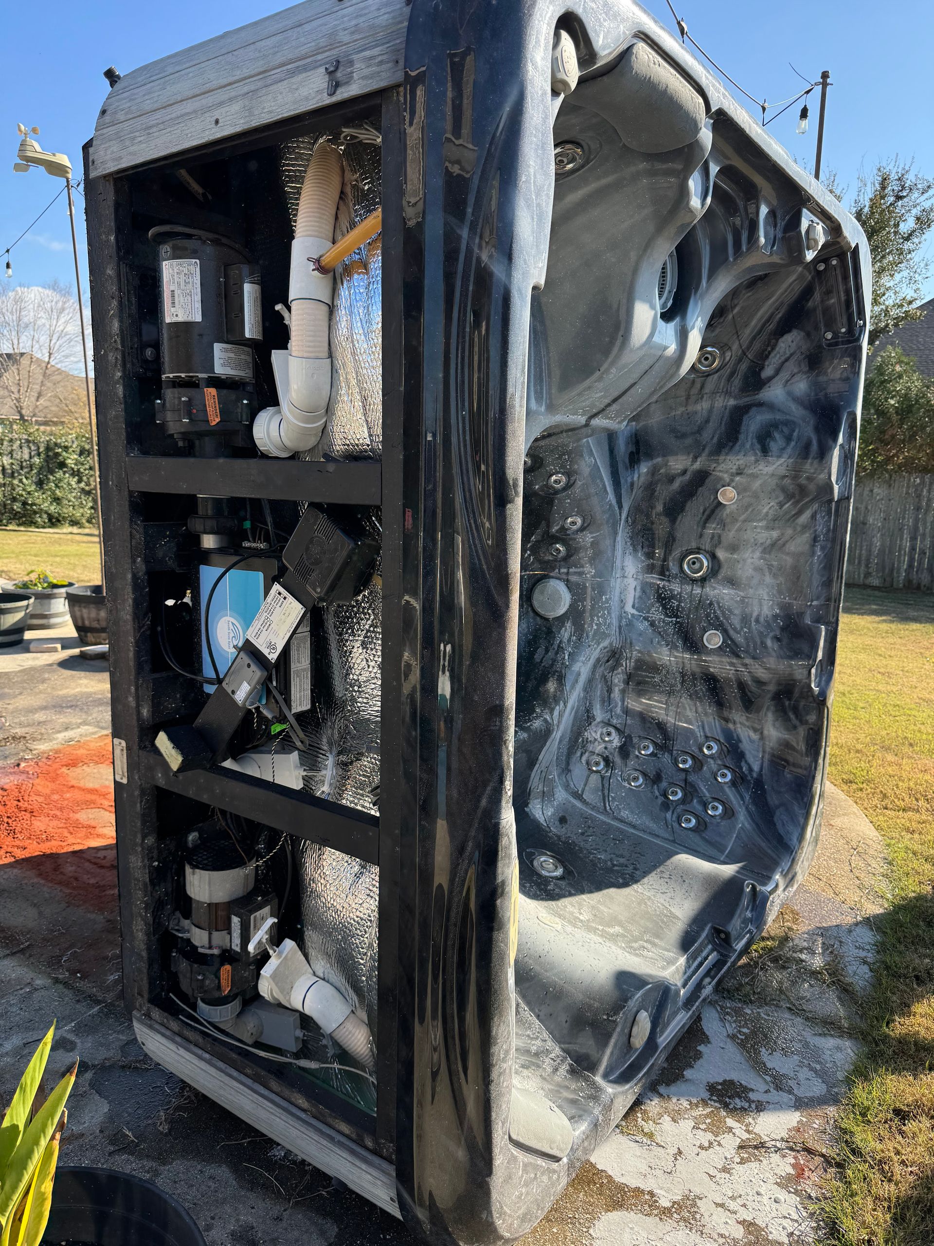 Damaged black equipment cabinet with exposed interior components outdoors beside a tree and orange debris