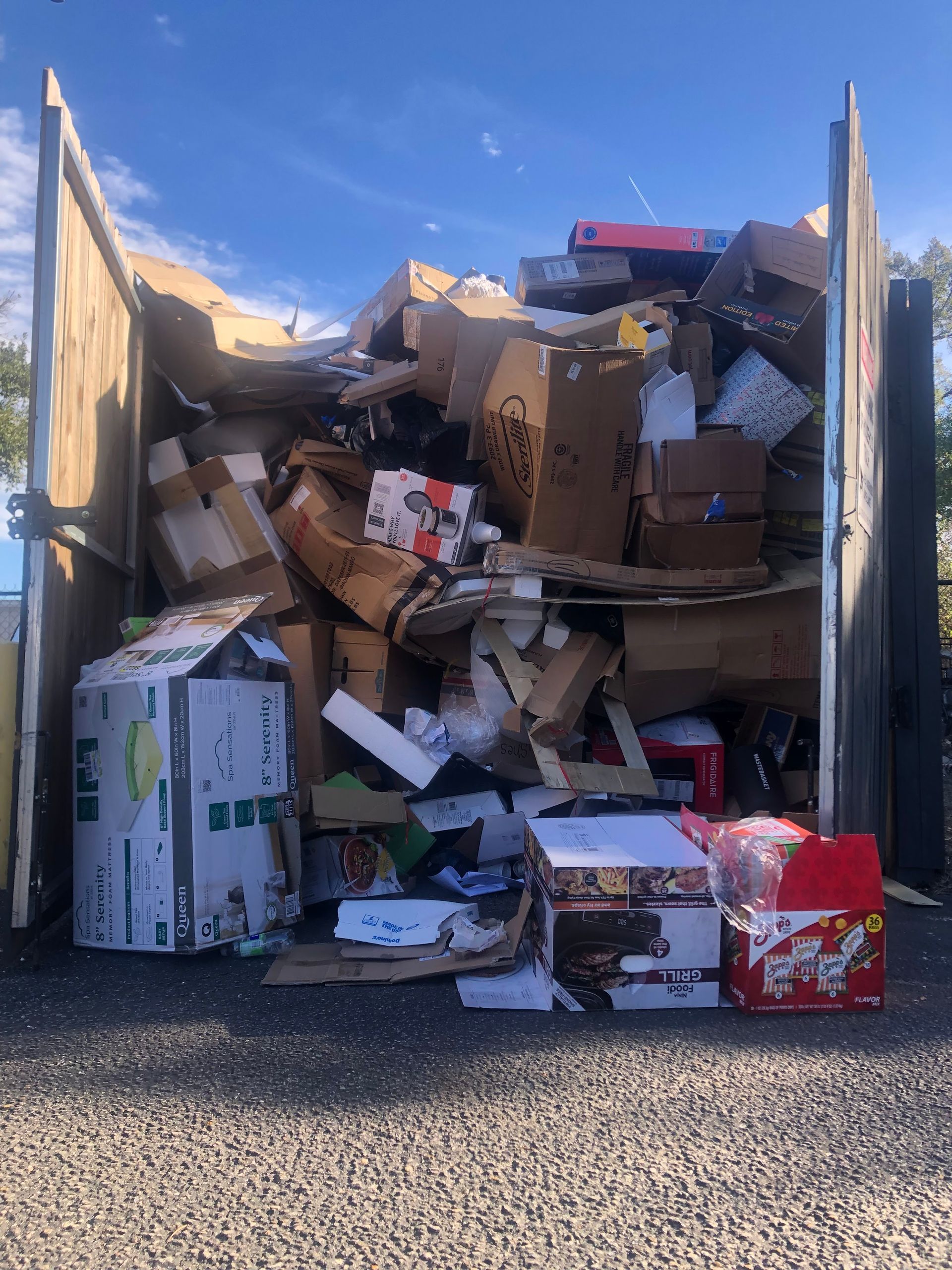 Overflowing dumpster with cardboard and mixed trash, packed to the top in an outdoor lot